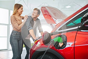 Young smiling family buying first electric car in the showroom. Attractive couple are enjoy to buy an eco-friendly car