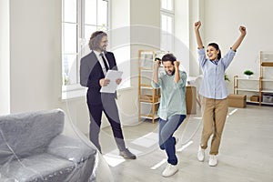 Young smiling family couple happy about buying a new apartment standing with man realtor.