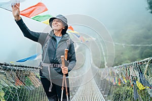 Young smiling female crossing canyon over Suspension Bridge and touching multicolored Tibetan Prayer flags hinged over gorge. Mera