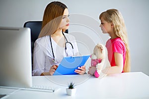 Young smiling female doctor and her little patient with teddy be