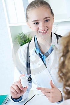 Young smiling female doctor hold in arms pill bottle and offer it to visitor. Antidepressant or vitamins for healthy