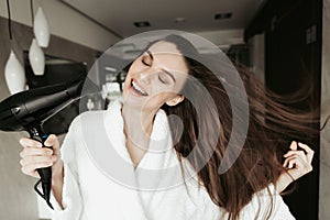 Young smiling female drying hair with blowdryer