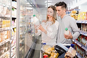 Young smiling female and male customers choosing milk and dairy products in grocery, family shopping