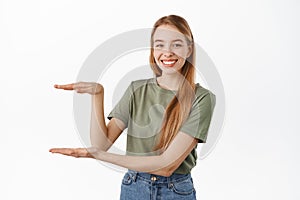 Young smiling female model showing an item, holding something, empty space between hands, looking pleased, recommending