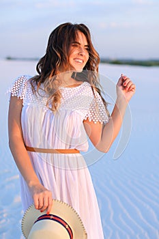 Young smiling female person standing on white sand, wearing dres