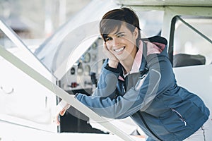 Young smiling female pilot leaning on a plane