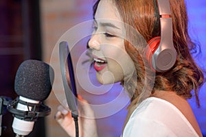 Young smiling female singer wearing headphones with a microphone while recording song in a music studio with colorful lights