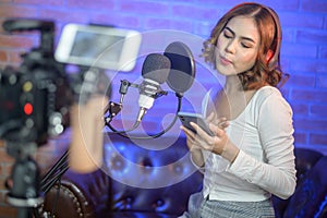 Young smiling female singer wearing headphones with a microphone while recording song in a music studio with colorful lights