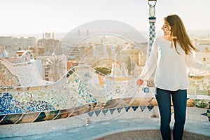 Young smiling female tourist spending vacation in Barcelona,Catalonia,Spain.Traveling to Europe,visiting Parc Guell.Best sunrise