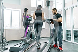 Young smiling fitness women with personal trainer an adult athletic man on treadmill in the gym. Sport, teamwork, training,