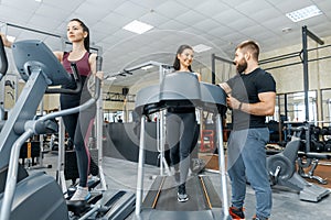 Young smiling fitness women with personal trainer an adult athletic man on treadmill in the gym. Sport, teamwork, training,