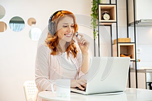 Young smiling friendly ginger girl working as agent at call center from home while drinking coffee.