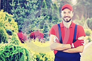 Young smiling gardener with crossed arms standing in garden