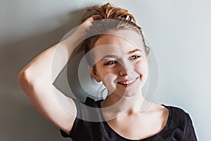 A young smiling girl adjusts her hair with her hand against the blue wall