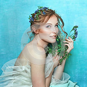 Young smiling girl with blue flowers on light blue background. Spring beauty portrait