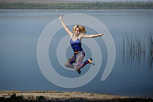 Young smiling girl in colored leggings and blue top on heels jumps on a river shore