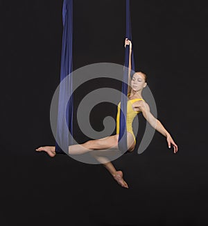 Young, smiling girl doing exercises on a loop of aerial silk