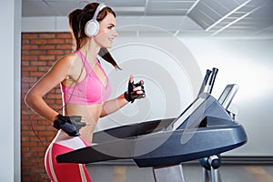 Young smiling girl with headphones running on a treadmill in a sport club. The concept of sport and active lifestyles