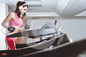 Young smiling girl with headphones running on a treadmill in a sport club. The concept of sport and active lifestyles