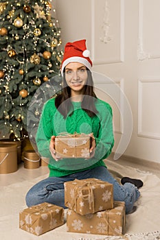 The young smiling girl hold brown gift near Christmas festive tree
