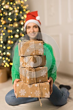 The young smiling girl hold brown gifts near Christmas festive tree