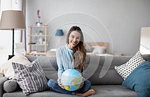 Young smiling girl holding a globe while sitting on the sofa at home