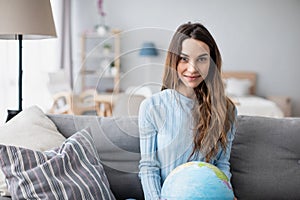 Young smiling girl holding a globe while sitting on the sofa at home