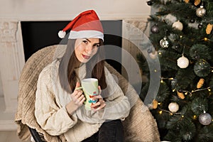 The young smiling girl holding a green cup of cacao near Christmas festive tree