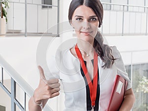 Young Smiling Girl Made Successful Work Shows Gesture Big Thumb Up. Beautiful Smiling Businesswoman Standing Against White Offices