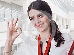 Young Smiling Girl Made Successful Work Shows Gesture Big Thumb Up. Beautiful Smiling Businesswoman Standing Against White Offices