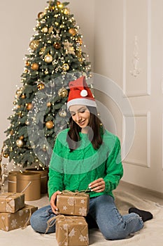 The young smiling girl opens brown gift near Christmas festive tree
