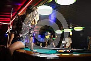 Young smiling girl playing billiard in club