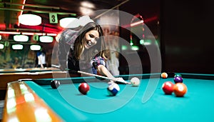 Young smiling girl playing billiard in club