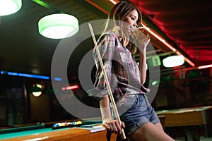 Young smiling girl playing billiard in club