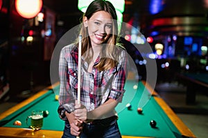 Young smiling girl playing billiard in club