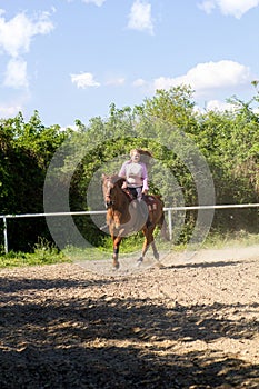 Young smiling girl riding her brown horse in a training field