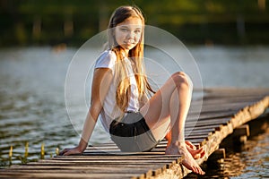 Young smiling girl sitting on pier in sunset beams