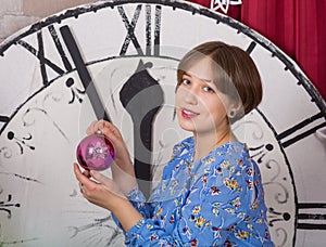Young smiling girl with toys. glass balls on the background of the New Year`s clock