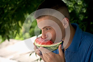 Young smiling guy eats a slice of watermelon
