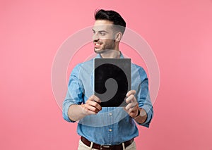 Young smiling guy looking to side and presenting tab