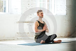 Young smiling guy sitting on a fitness mat and meditating
