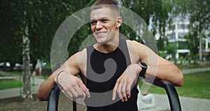 Young smiling handsome man with athletic body taking break at workout outdoors