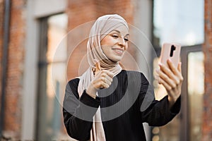 Young smiling happy muslim woman doing video call using smartphone at the city.