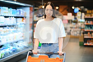 Young smiling happy woman 20s in casual clothes shopping at supermaket store with grocery cart