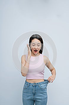 Young smiling happy woman show loose pants on waist after weightloss isolated on white background