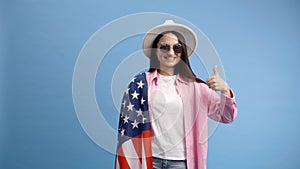 Young smiling happy woman wears casual clothes and white hat holding american flag and shows a finger up gesture isolated