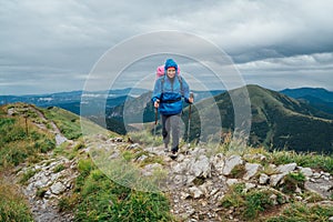 Young smiling hiker woman dressed rain suit walking by rocky Slovakian Mala Fatra mountain range using tracking poles with