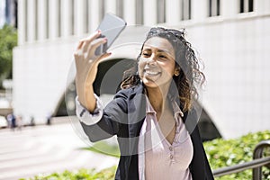 Young smiling hispanic american woman taking a selfie outdoors with her smart phone