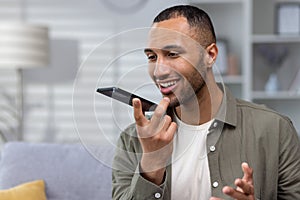 Young smiling hispanic man talking on the phone through the loudspeaker, recording the conversation. Close-up photo