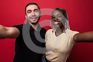 Young smiling interracial couple, caucaisan man and african woman taking selfie on mobile phone on red background